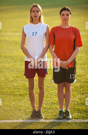 Two girls in a football uniform, stand on a football field waiting for penalty kick. They crossed their arms in front of them. Stock Photo