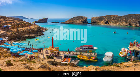 Comino, Malta - Tourists crowd at Blue Lagoon to enjoy the clear turquoise water on a sunny summer day with clear blue sky and boats on Comino island, Stock Photo