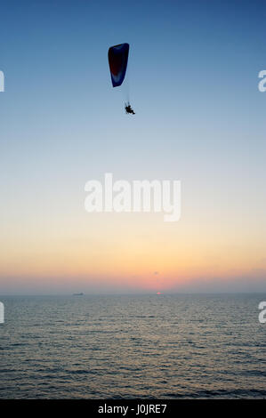 Powered paraglider flying over the sea at sunset sky background Stock Photo