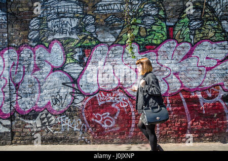 A man walks past a wall covered in street art and graffiti on Brick Lane in East London. Stock Photo