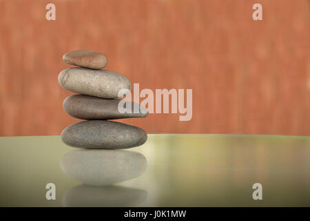 Four river rocks balanced on each other with salmon color background and greenish table. Stock Photo