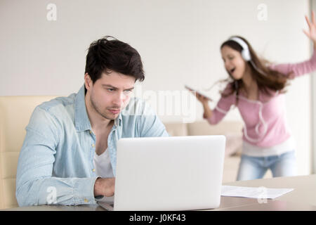 Annoyed man working on laptop, woman dancing in headphones indoo Stock Photo