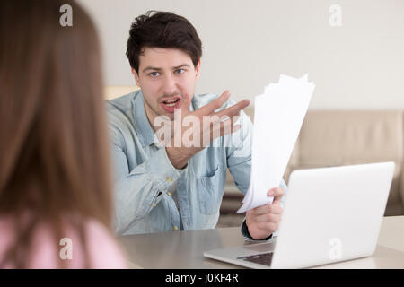 Angry man shouting at woman pointing at documents in hand Stock Photo