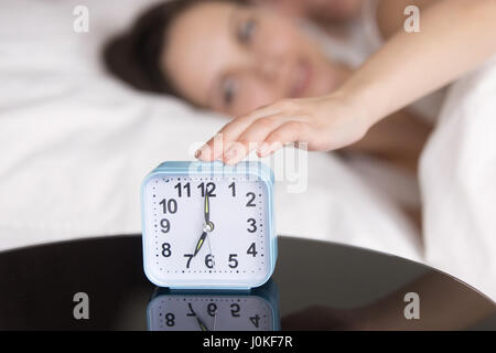 Young lady turning off ringing alarm clock in the morning Stock Photo