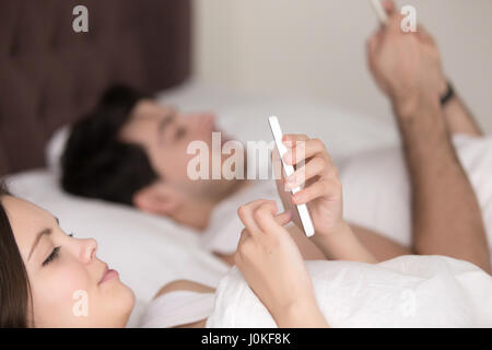 Closeup of young couple using mobile smartphones lying in bed Stock Photo