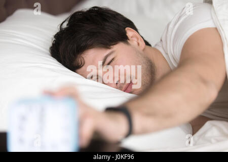 Sleepy man turning off alarm clock, time to wake up Stock Photo