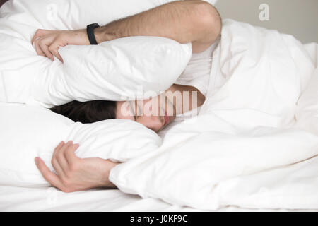 Young guy trying to sleep, covering his head with pillow  Stock Photo