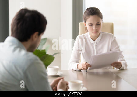 Serious businesswoman studying papers sitting opposite man at of Stock Photo