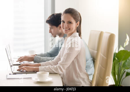 Happy young businesswoman looking at camera, working with male c Stock Photo