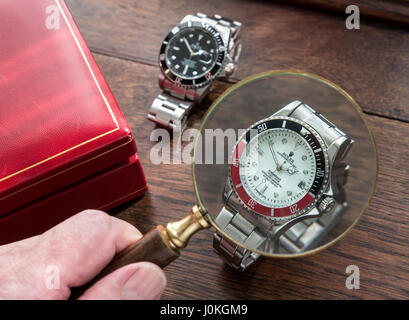 ROLEX FAKE WATCHES Magnifying glass and fake replica copy counterfeit men's Rolex watches on old wooden desk top with red leather watch case Stock Photo