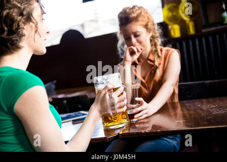 A couple of friends enjoying a beer together, focus on the glass of beer. Two girlfriends get together at the pub and spend some time chatting Stock Photo