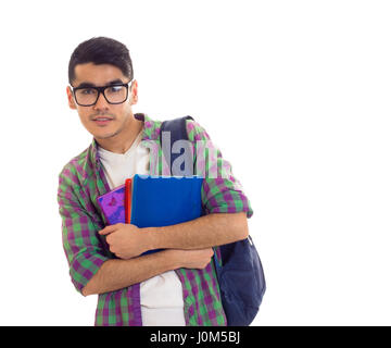 Young handsome man with black hair in white T-shirt and checkered shirt with blue backpack holding books on white background in studio Stock Photo