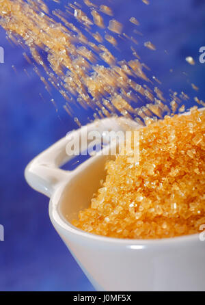 Pouring brown sugar crystals into a bowl. Close up view. Stock Photo
