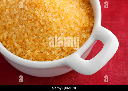 Brown sugar crystals in a bowl from above over red background Stock Photo