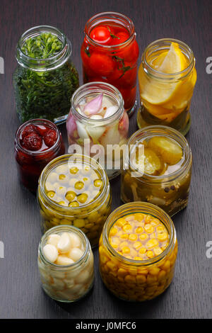 Opened jars with various preserved food on dark board Stock Photo