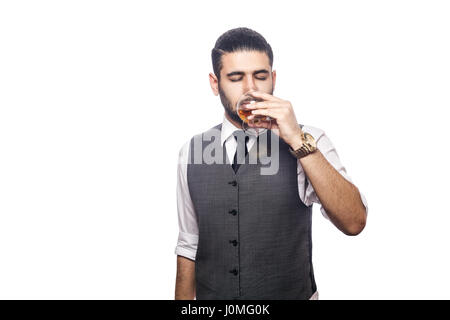 Handsome bearded businessman holding a glass of whiskey. drinking with closed eyes. studio shot, isolated on white background. Stock Photo