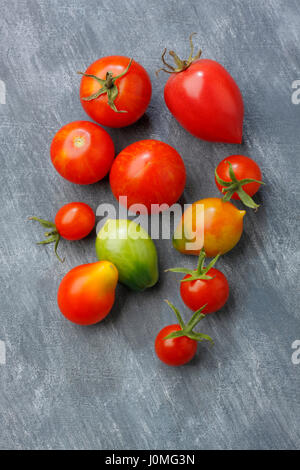 Variety of tomato fruits over painted textile background. Two fruits unripe. Overhead view. Stock Photo