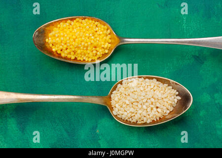 Two silver spoons filled with millet groats and sesame seeds. Close up, top view. Stock Photo