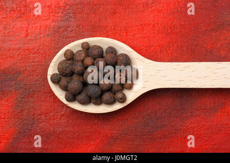 Allspice (Pimenta dioica) berries on wooden spoon over red painted textile background Stock Photo