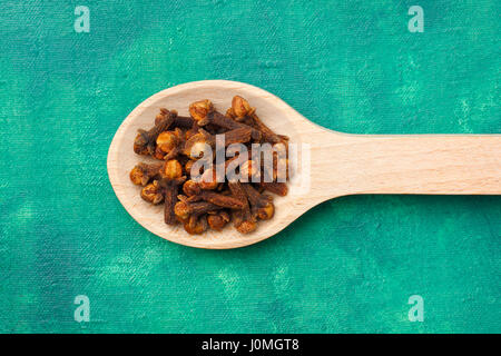 Cloves (Syzygium aromaticum) dried flower buds on wooden spoon over emerald painted textile background Stock Photo