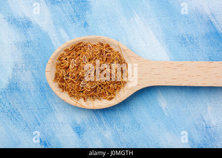 Dill (Anethum graveolens) seeds on wooden spoon over blue painted textile background Stock Photo