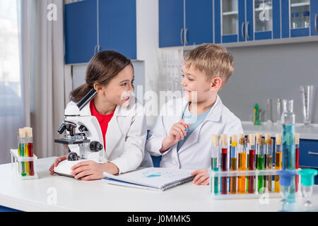 Little boy and girl in white coats using microscope and looking at each other in lab Stock Photo