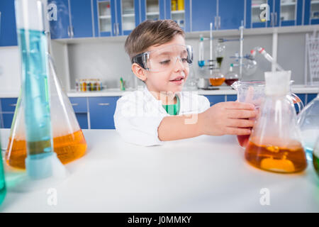 Little boy in protective glasses making experiment in chemical laboratory