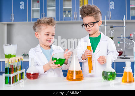 Smiling little boys in lab coats making experiment in chemical laboratory Stock Photo