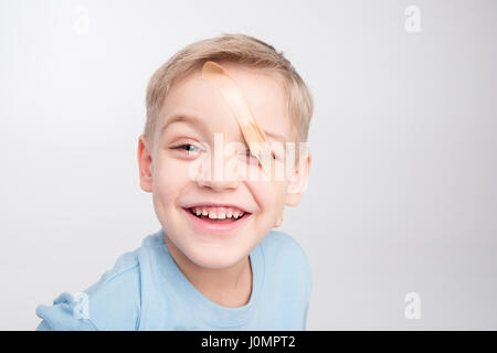 Cute little boy with patch on his eye looking at camera and laughing on white Stock Photo