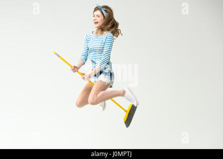 Happy beautiful young woman flying on broom on grey Stock Photo