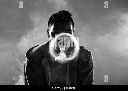 Black and white photo of young bearded man vaping and making circle from smoke Stock Photo