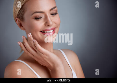 Nice middle aged woman  applying face cream, joyfully smiling Stock Photo