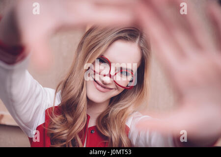 Stylish hipster woman with red eyeglasses making focus framing gesture Stock Photo