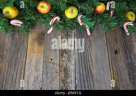 apples and candy canes in Christmas pine garland on weathered wood Stock Photo