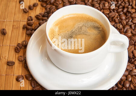 Fresh cup of coffee surrounded by coffee beans on a wooden background Stock Photo