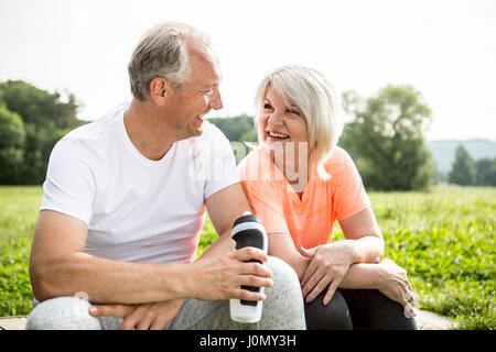 Mature couple sitting outdoors resting, man holding water bottle. Stock Photo