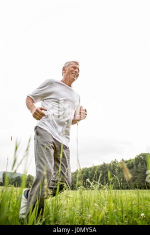 Senior man jogging in grass. Stock Photo