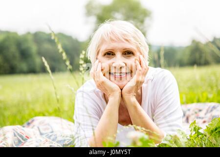 Senior woman lying on grass with hands on chin. Stock Photo
