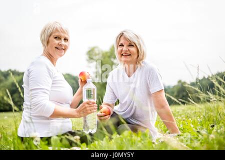 Two women sitting on grass with apples and water. Stock Photo