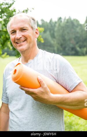 Man with yoga mat, smiling. Stock Photo