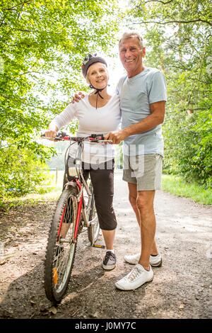 Mature woman on bike, senior man with arm around. Stock Photo