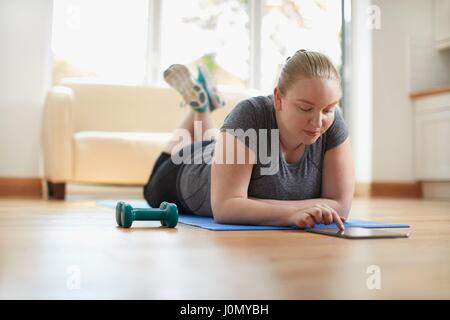 Young woman lying on yoga mat using digital tablet. Stock Photo