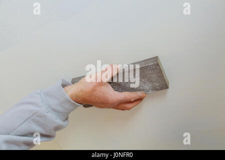 plastering man hand sanding the plaste in drywall seam plasterboard sanding the wall Stock Photo