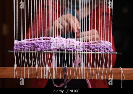 close up of hands weaving fabric through vertical loom Stock Photo