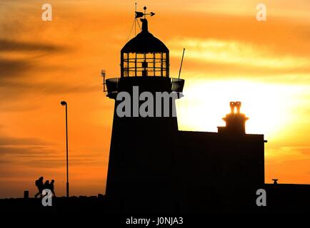 People go for an early morning walk along Howth pier, Dublin, as the sun rises. Stock Photo
