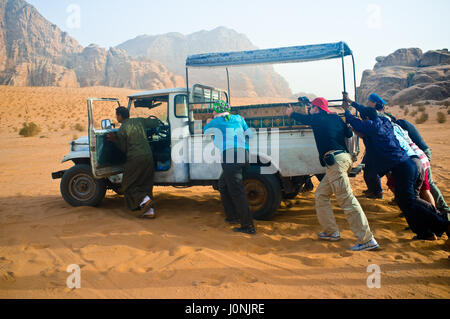 People pushing a damaged car in the middle of nothing. Wadi Rum desert. Jordan. Stock Photo