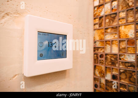 Thermostat with LCD display of the warm floor on the wall in the bathroom. Stock Photo