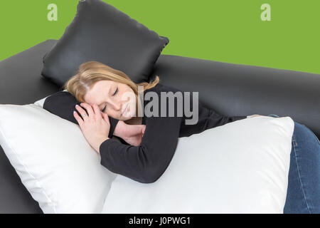 Young woman is sleeping on the black and white couch with black and white pillows. Trendy green wall in the background. Stock Photo