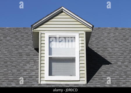 Classical vertical roof window with white frame on the roof gray asphalt roofing shingles on a background of blue sky. Stock Photo