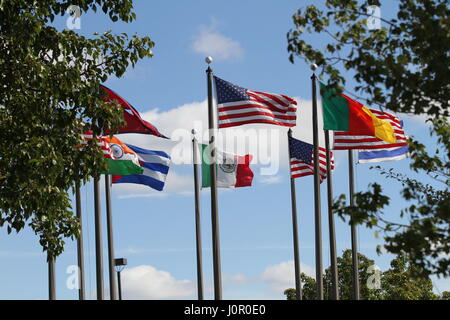 The flags US, Nepal, Cameroon,  Israel, India, Mexico and Cuba on a flagpoles blowing in the wind against a blue sky and white clouds. The wind blows. Stock Photo